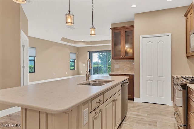 kitchen with sink, hanging light fixtures, appliances with stainless steel finishes, a kitchen island with sink, and backsplash