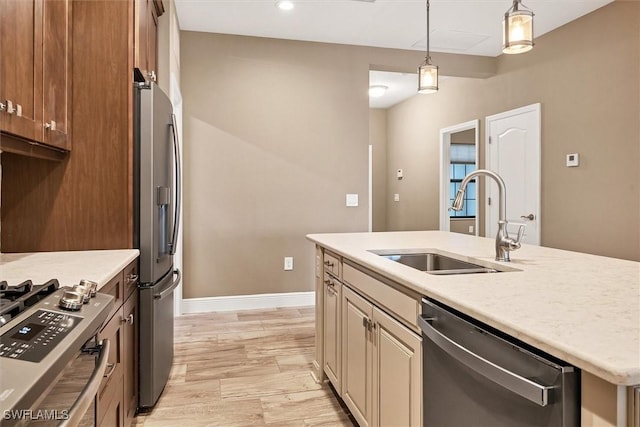 kitchen with an island with sink, sink, hanging light fixtures, stainless steel appliances, and light hardwood / wood-style flooring