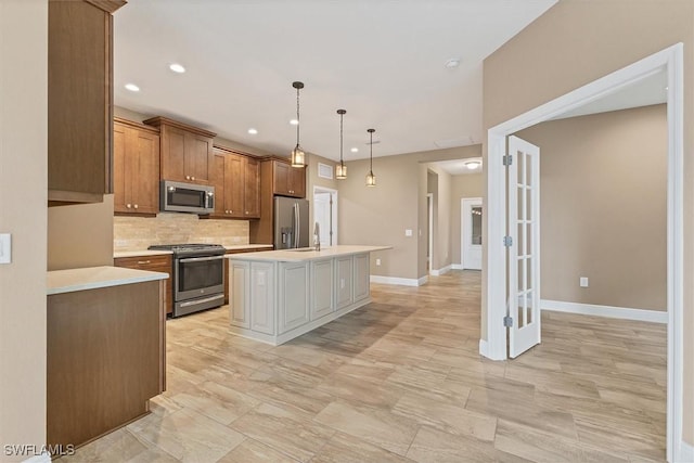 kitchen featuring appliances with stainless steel finishes, decorative light fixtures, an island with sink, and backsplash