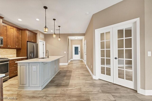 kitchen with appliances with stainless steel finishes, pendant lighting, sink, backsplash, and a kitchen island with sink