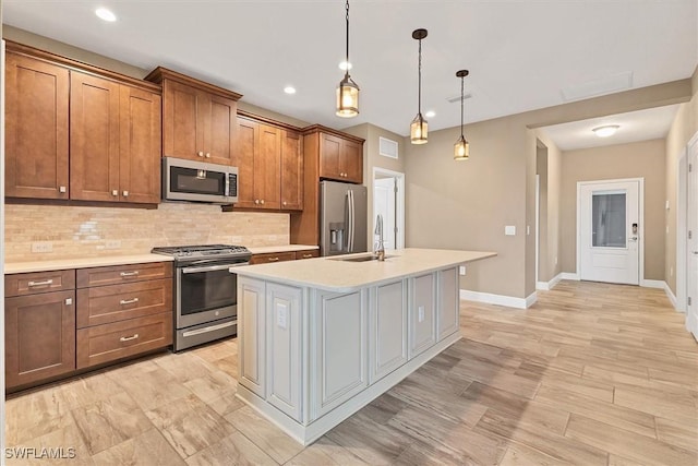 kitchen with sink, stainless steel appliances, tasteful backsplash, an island with sink, and decorative light fixtures