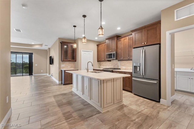 kitchen with sink, a kitchen island with sink, backsplash, hanging light fixtures, and stainless steel appliances