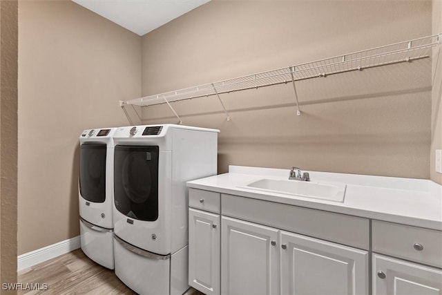 clothes washing area with cabinets, sink, washing machine and dryer, and light wood-type flooring