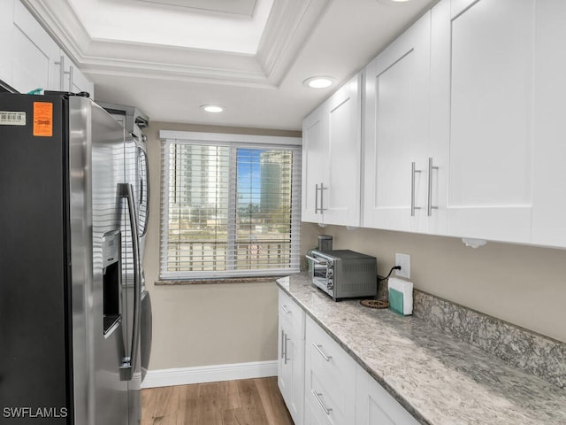 kitchen featuring stainless steel fridge, light wood-type flooring, ornamental molding, light stone counters, and white cabinetry