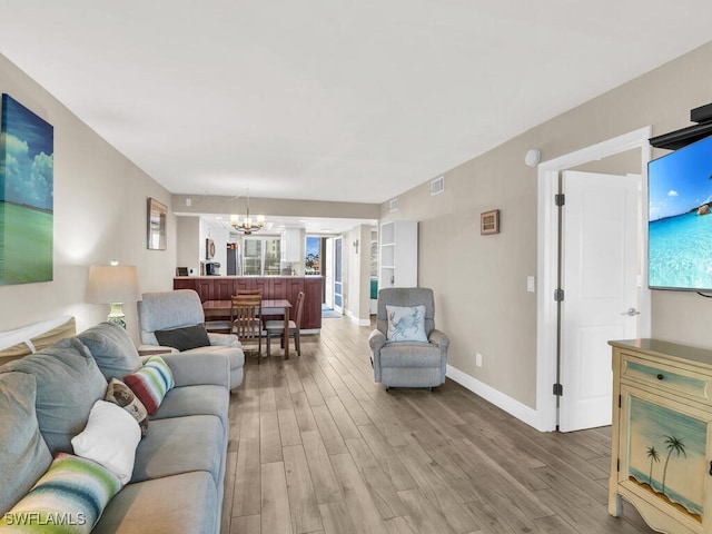 living room featuring light wood-type flooring, built in features, and a notable chandelier