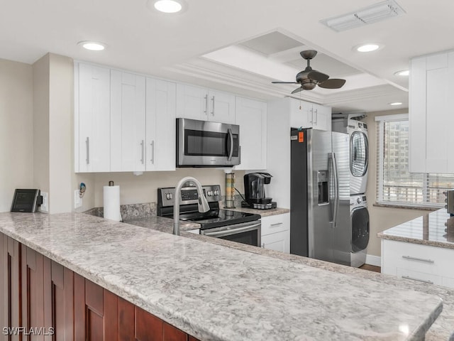 kitchen featuring white cabinets, a raised ceiling, stacked washer and dryer, ceiling fan, and stainless steel appliances