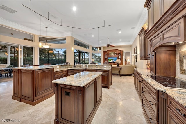 kitchen featuring ceiling fan, light stone countertops, decorative light fixtures, black electric cooktop, and a kitchen island