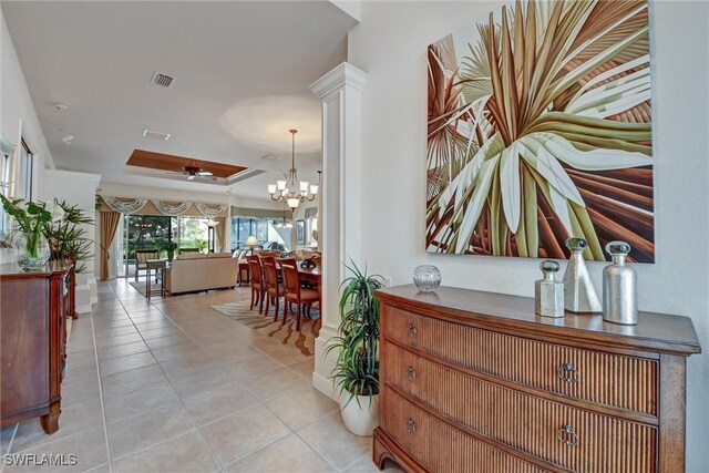 hall featuring a raised ceiling, light tile patterned floors, and an inviting chandelier