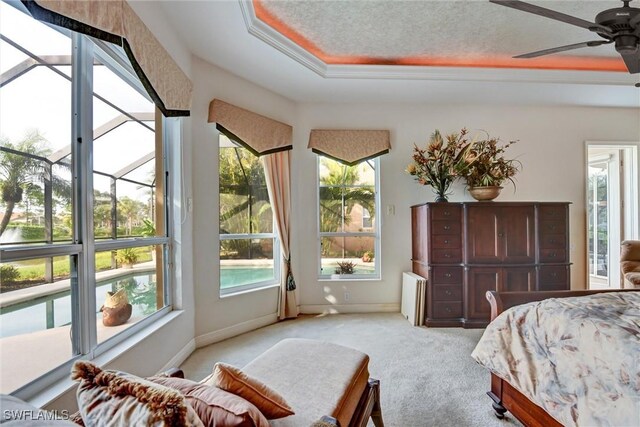 bedroom with multiple windows, light colored carpet, a raised ceiling, and ceiling fan