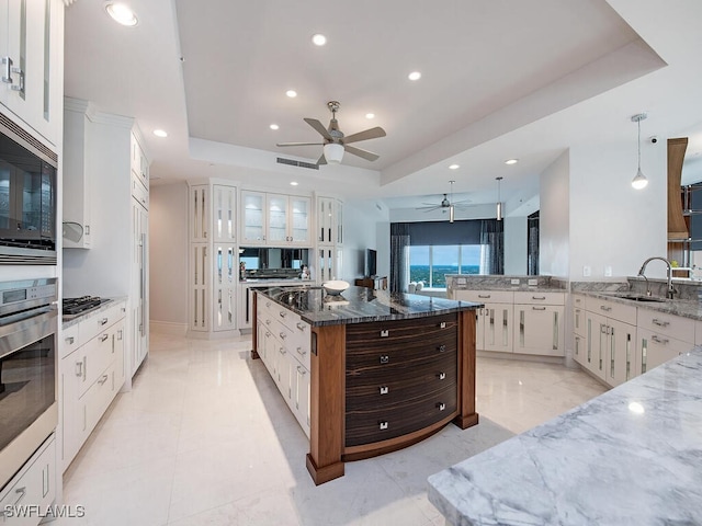 kitchen with stainless steel oven, sink, a raised ceiling, dark stone counters, and white cabinets