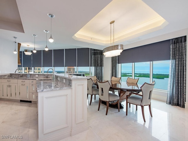 kitchen with white cabinets, pendant lighting, a water view, and a raised ceiling