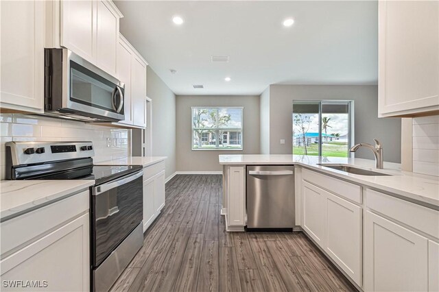 kitchen with light stone counters, stainless steel appliances, white cabinetry, and sink