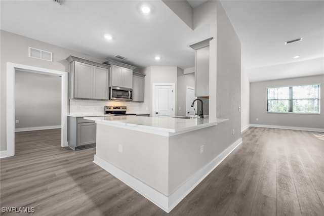 kitchen featuring appliances with stainless steel finishes, gray cabinetry, a sink, tasteful backsplash, and wood finished floors
