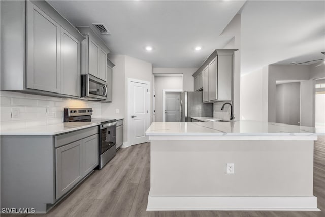 kitchen with stainless steel appliances, gray cabinetry, a sink, backsplash, and a peninsula