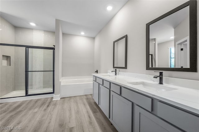 bathroom with wood finished floors, a shower stall, a bath, double vanity, and recessed lighting