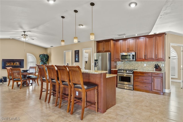 kitchen featuring hanging light fixtures, decorative backsplash, ceiling fan, light stone countertops, and appliances with stainless steel finishes