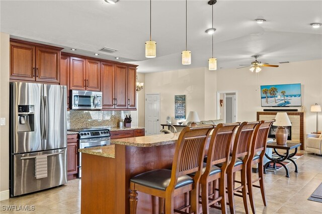 kitchen featuring decorative backsplash, a breakfast bar, stainless steel appliances, ceiling fan, and hanging light fixtures