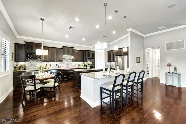 kitchen featuring a spacious island, stainless steel appliances, decorative light fixtures, and light stone counters