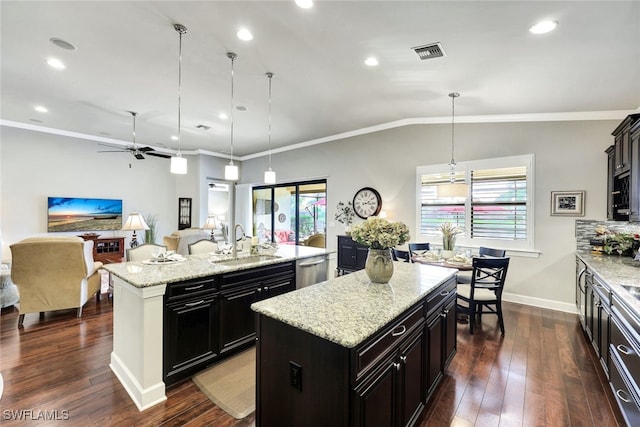 kitchen featuring a kitchen island with sink, sink, pendant lighting, and light stone counters