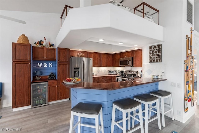 kitchen featuring a kitchen breakfast bar, wine cooler, light wood-type flooring, kitchen peninsula, and stainless steel appliances