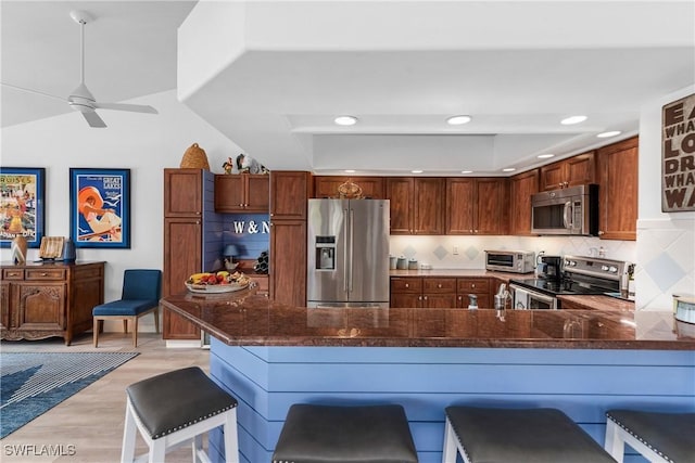 kitchen featuring ceiling fan, stainless steel appliances, a kitchen breakfast bar, backsplash, and kitchen peninsula