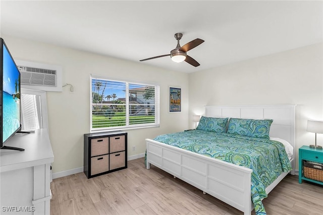 bedroom with a wall mounted AC, light hardwood / wood-style flooring, and ceiling fan