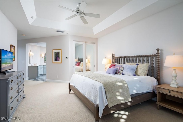 carpeted bedroom featuring ensuite bathroom, ceiling fan, and a tray ceiling