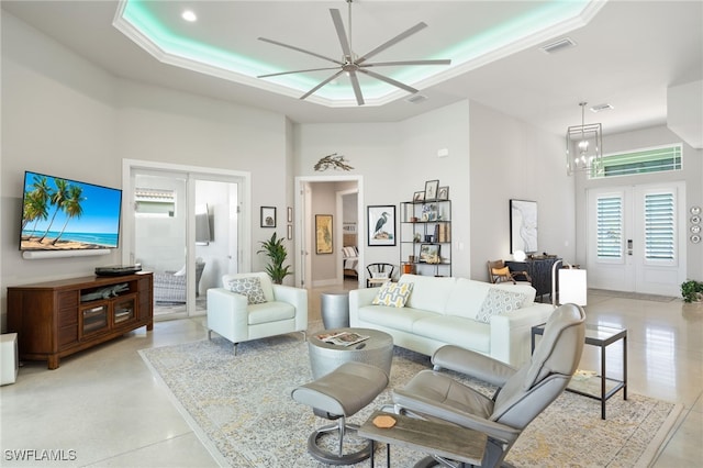 living room with french doors, a raised ceiling, and ceiling fan with notable chandelier