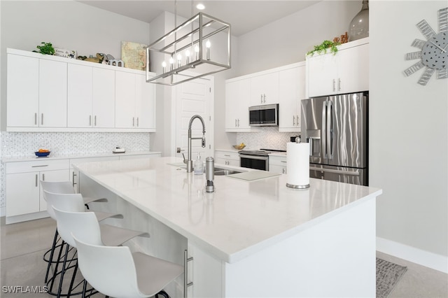 kitchen with stainless steel appliances, white cabinetry, hanging light fixtures, and a center island with sink