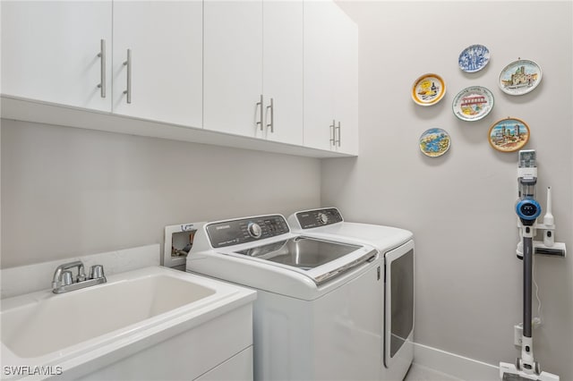 clothes washing area with separate washer and dryer, sink, and cabinets