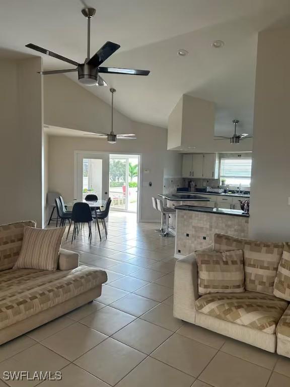 tiled living room with ceiling fan and high vaulted ceiling