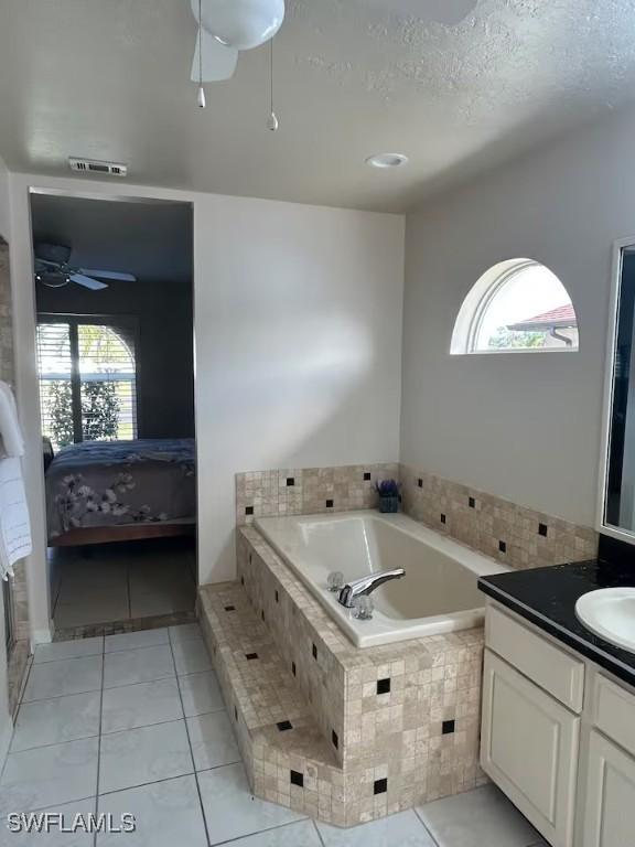 bathroom with tile patterned flooring, vanity, a textured ceiling, and tiled tub