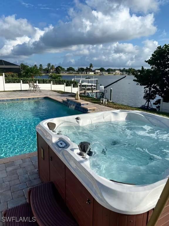 view of pool featuring pool water feature, a boat dock, a water view, a patio, and a hot tub