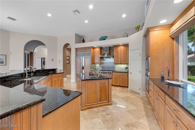 kitchen with wall chimney exhaust hood, a kitchen island, sink, and dark stone counters