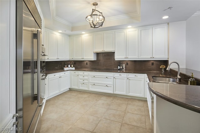 kitchen with stainless steel built in refrigerator, sink, white cabinetry, decorative light fixtures, and a raised ceiling