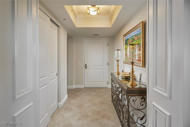 corridor with ornamental molding and a raised ceiling