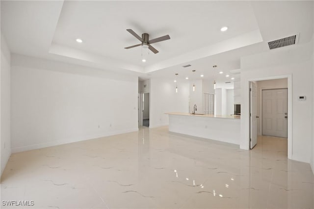 unfurnished living room with a tray ceiling, ceiling fan, and sink