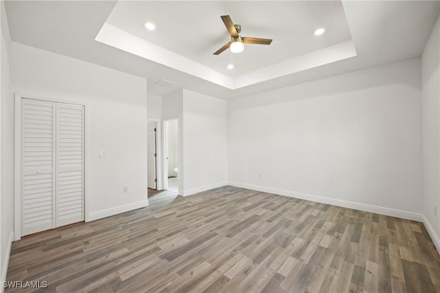 unfurnished bedroom with hardwood / wood-style flooring, ceiling fan, a closet, and a tray ceiling