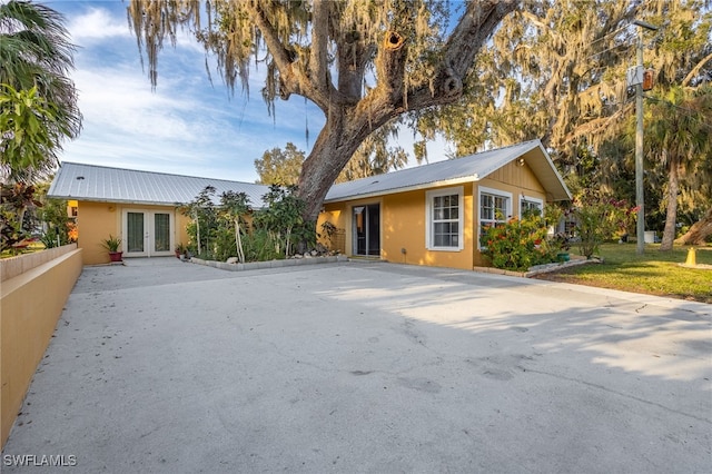 view of front of home featuring stucco siding, french doors, fence, and metal roof