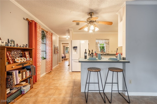 kitchen featuring visible vents, a ceiling fan, white fridge with ice dispenser, a breakfast bar area, and light tile patterned floors