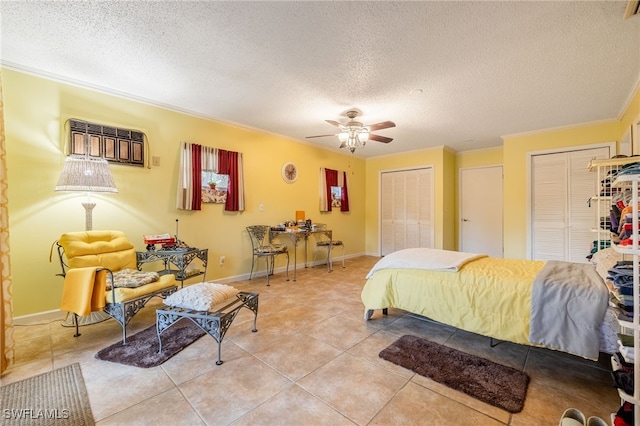 bedroom with a textured ceiling, light tile patterned floors, two closets, and ornamental molding