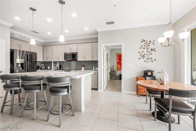 kitchen with gray cabinetry, pendant lighting, decorative backsplash, an island with sink, and appliances with stainless steel finishes