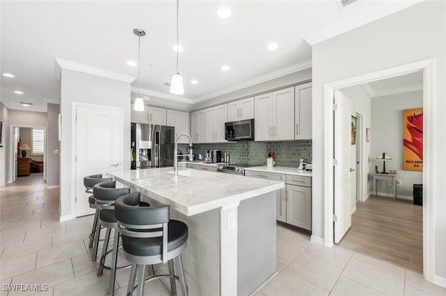 kitchen featuring a kitchen bar, a center island with sink, appliances with stainless steel finishes, decorative light fixtures, and light stone counters