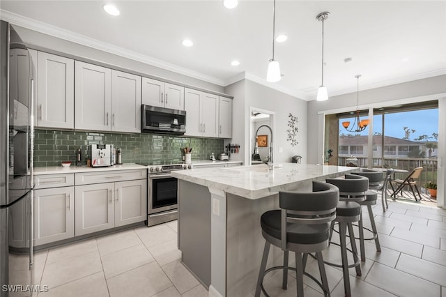 kitchen with light stone counters, stainless steel appliances, a kitchen island with sink, sink, and decorative light fixtures