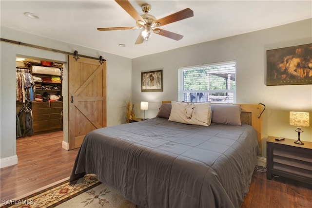 bedroom featuring a spacious closet, a closet, ceiling fan, a barn door, and hardwood / wood-style floors