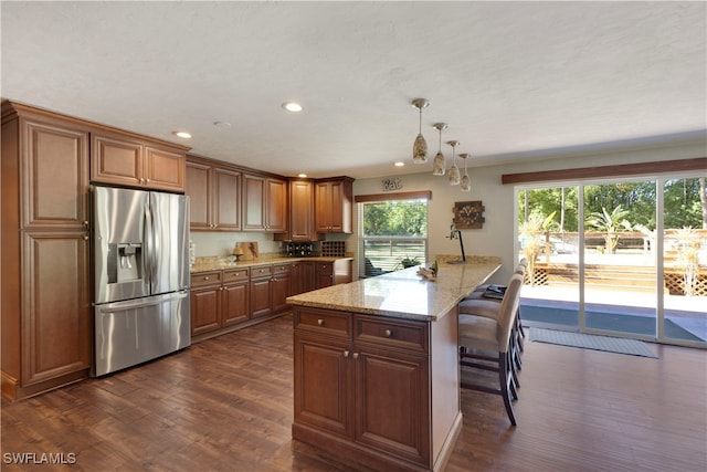 kitchen with dark wood-type flooring, a breakfast bar area, light stone counters, stainless steel fridge, and pendant lighting