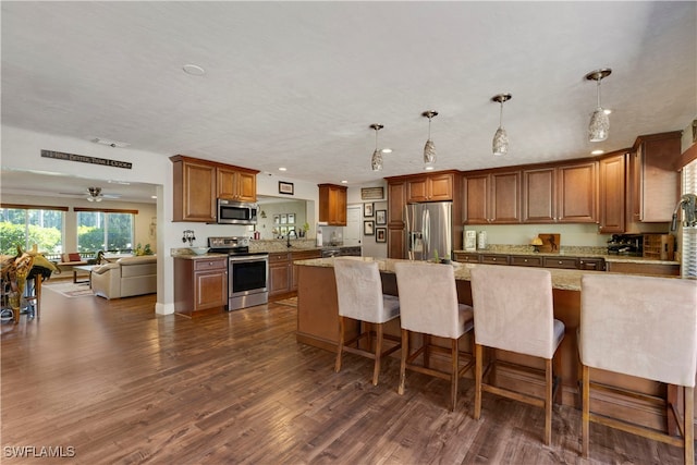 kitchen featuring pendant lighting, dark wood-type flooring, ceiling fan, stainless steel appliances, and light stone countertops