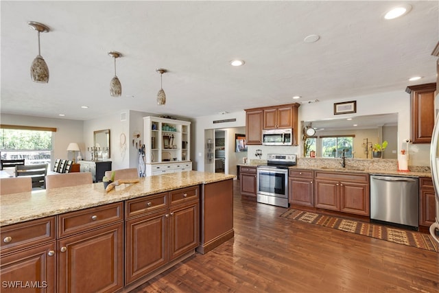 kitchen with sink, dark hardwood / wood-style flooring, hanging light fixtures, light stone counters, and stainless steel appliances