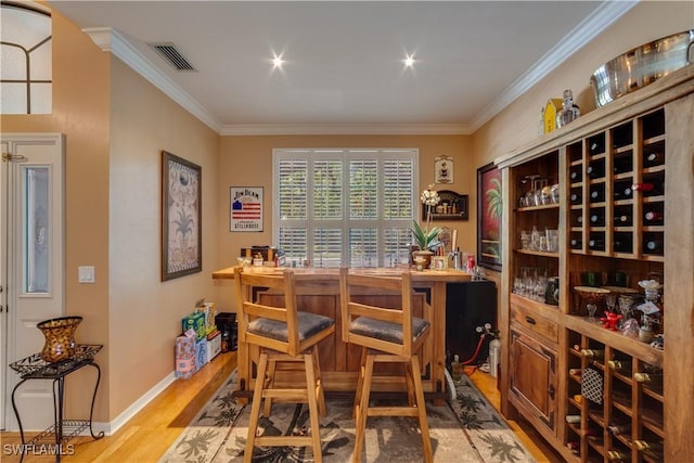 wine room with hardwood / wood-style floors, ornamental molding, and bar