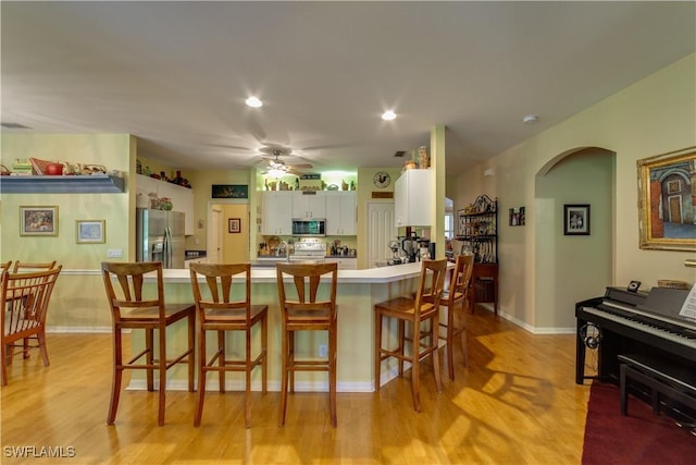 kitchen with a kitchen bar, stainless steel appliances, ceiling fan, white cabinets, and light hardwood / wood-style floors